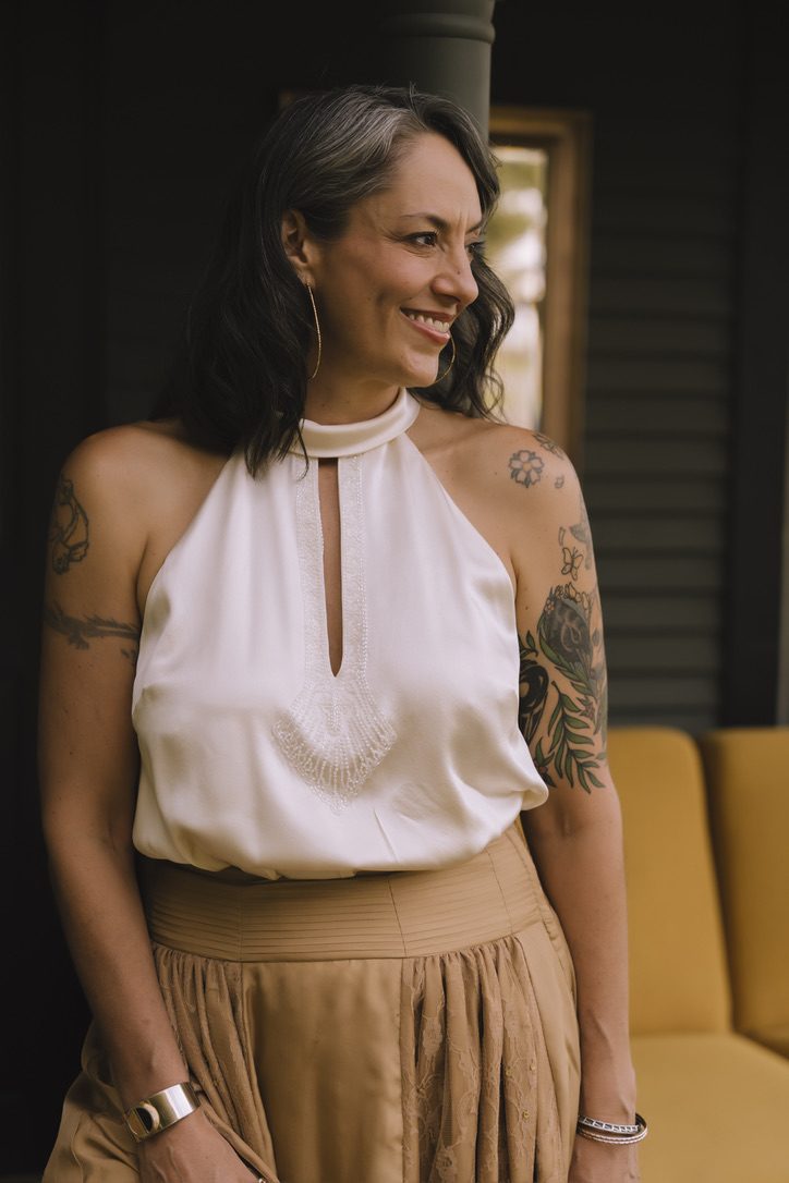 Camille Zenobia smiling on a porch in a white satin halter top